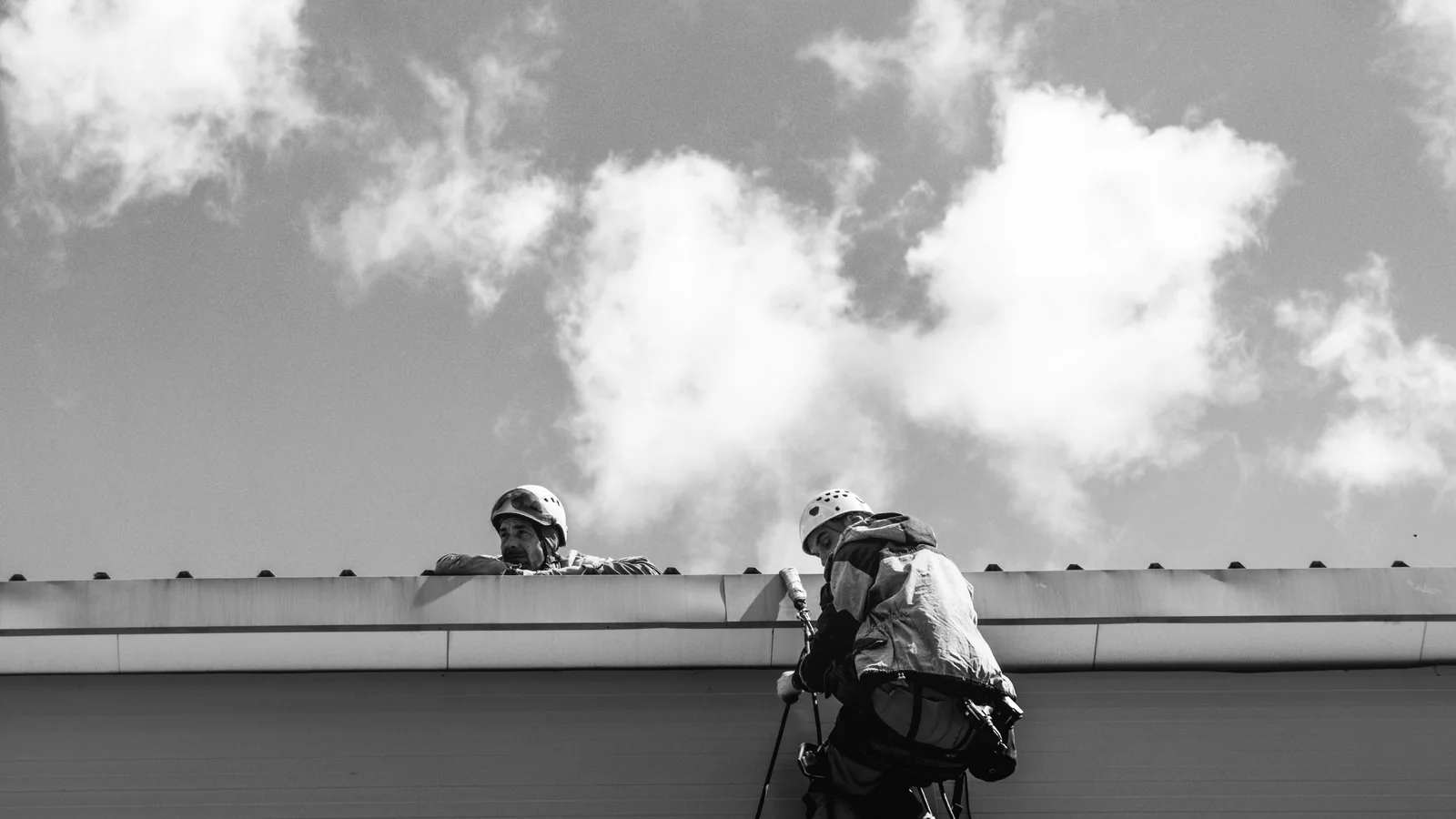 Roof professionals wearing helmets and fall protection during a rooftop inspection