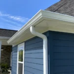 White seamless gutter and downspout installed on a blue North Carolina home